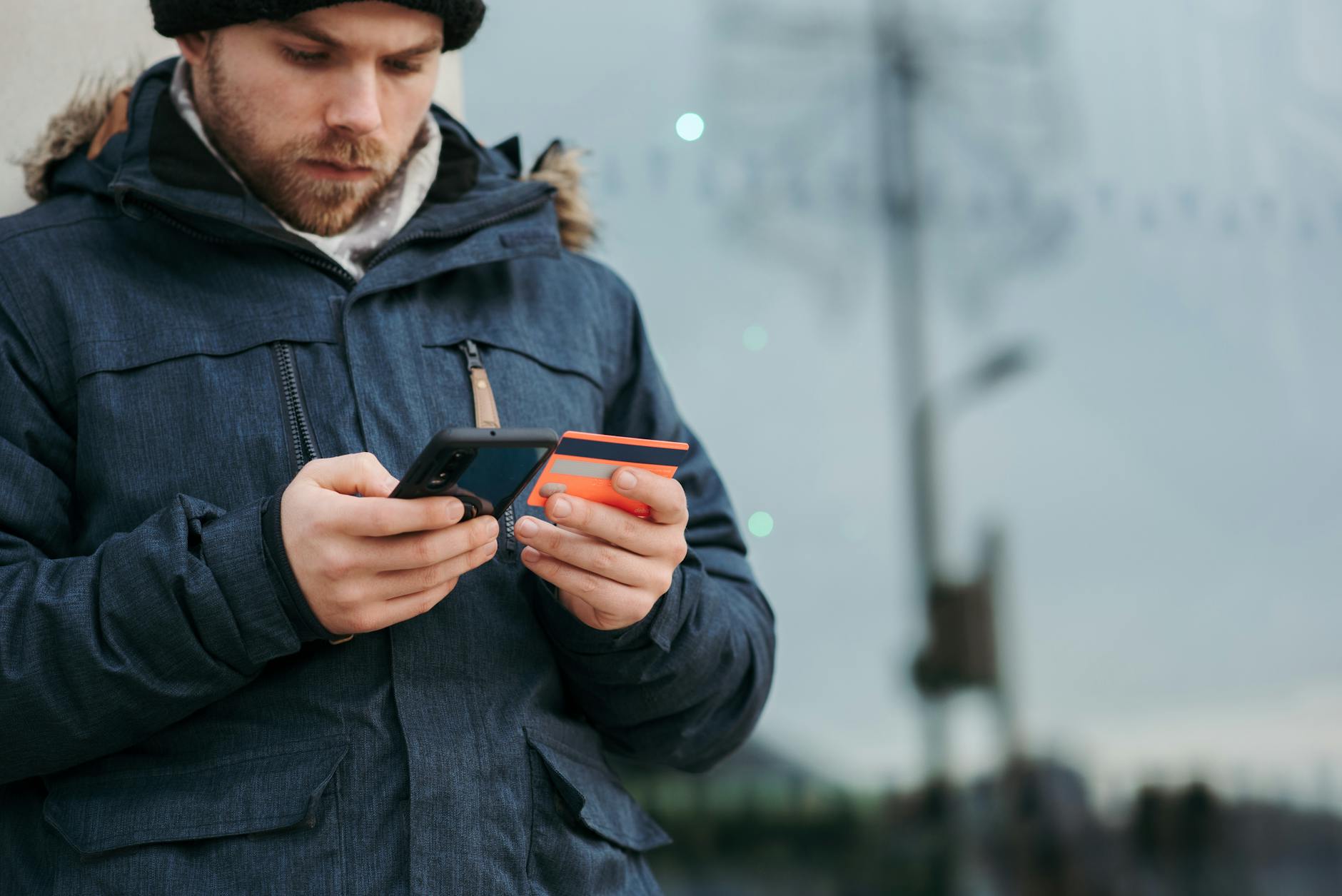 pensive man holding credit card and browsing smartphone on street in daytime